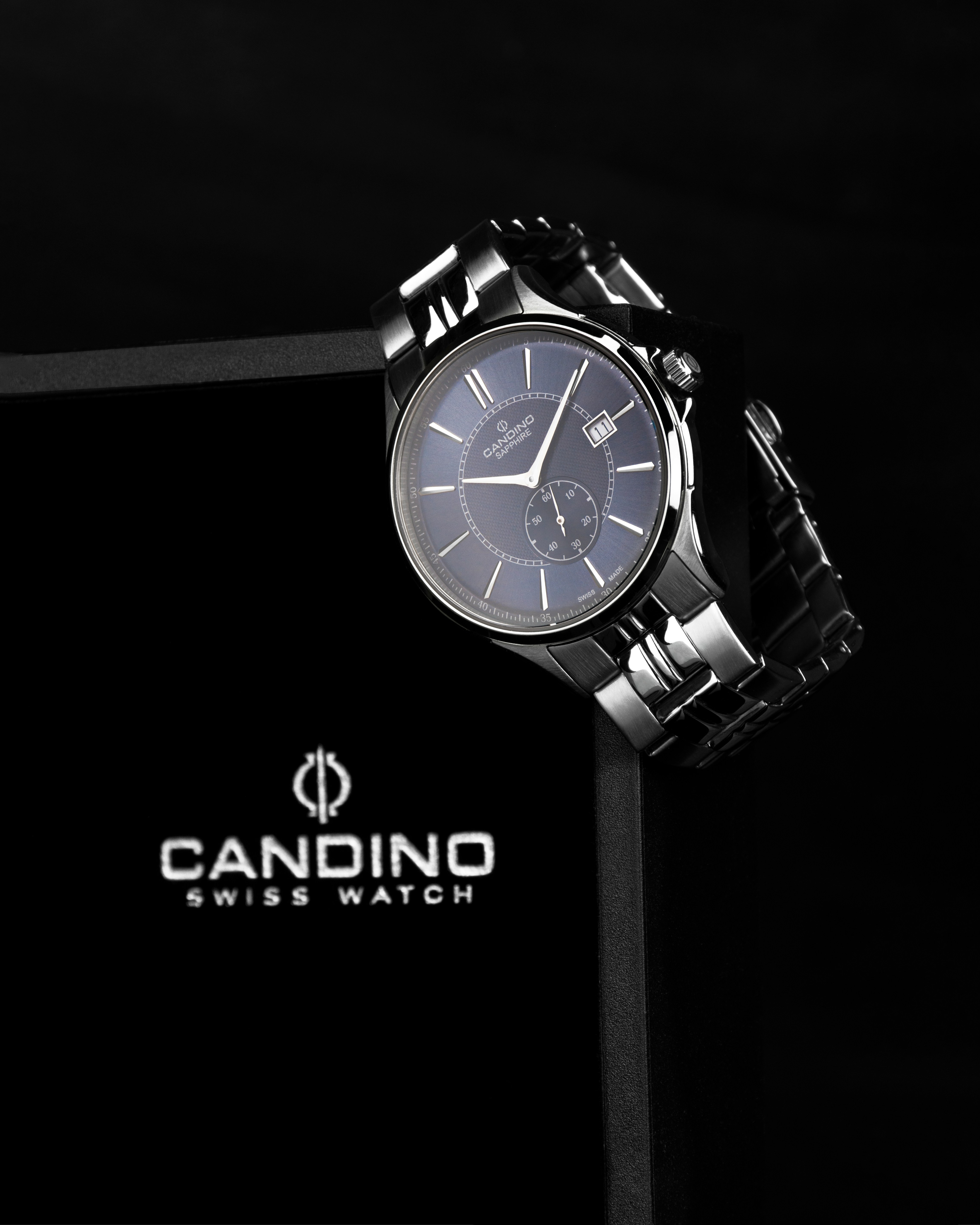 Montre mécanique argentée à cadran bleu, posée sur un écrin noir